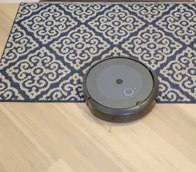 A modern robotic vacuum cleaning a stylish patterned carpet on a wooden floor.