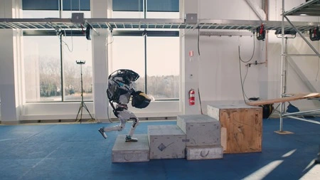 Atlas robot jumping over boxes to deliver tools to a worker.