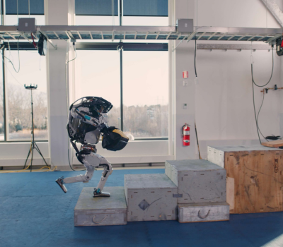 Atlas robot jumping over boxes to deliver tools to a worker.